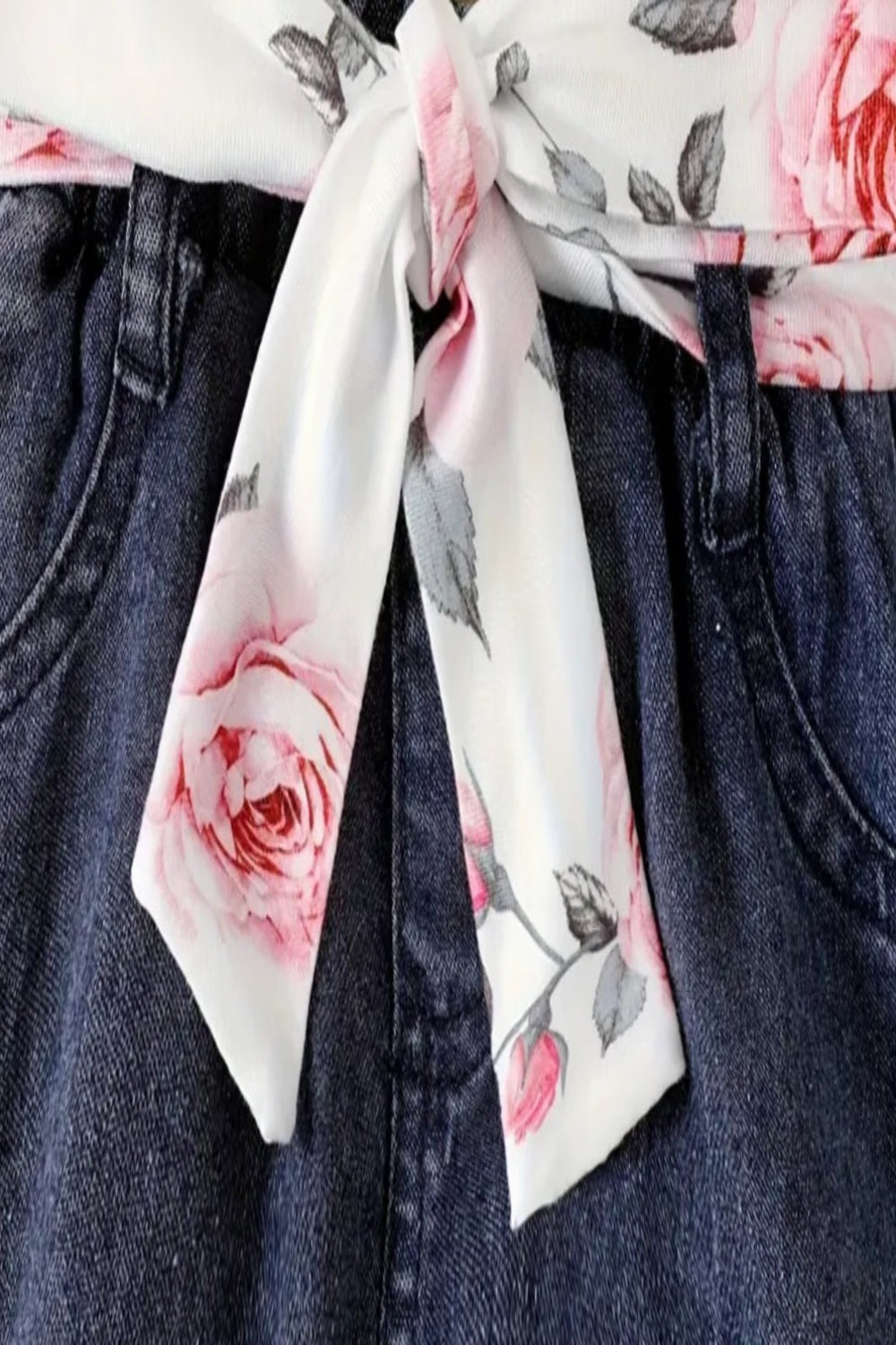 witte body met lange mouw met roze rozen en roze gilet en donkere  jeans met bijpassend riem